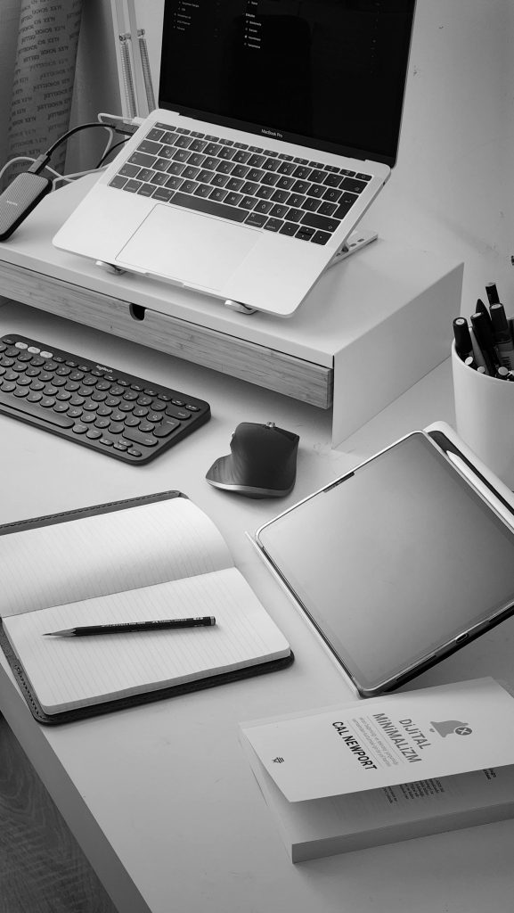 Black and white photo of a sleek office desk with digital devices and open notebook.
